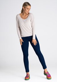 Jasnobeżowa bluzka z długim rękawem i okrągłym dekoltem, w połączeniu z ciemnoniebieskimi jeansami o slim fit oraz wielokolorowymi butami na platformie z zieloną podeszwą.