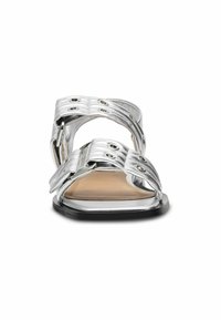 Silberne metallische Sandalen mit mehreren verstellbaren Riemen und kreisförmigen Perforationen, ausgestattet mit einer flachen Sohle und einem glatten, minimalistischen Design.