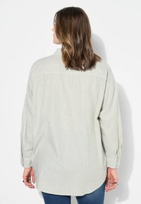 Light striped button-up shirt in soft fabric, featuring a back yoke, relaxed fit, and long sleeves with buttoned cuffs. Visible stitching details.