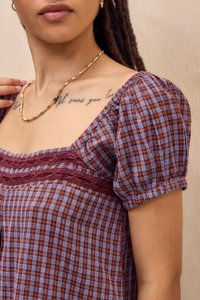 Kratki rukavi, majica sa kvadratnim dekolteom u ljubičastom i burgundskom kariranom materijalu sa teksturiranim čipkastim detaljima duž bust-a i napuhanim rukavima.