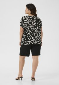 Top negro con flores blancas y rosas, combinado con pantalones cortos negros. El top tiene mangas cortas y un corte relajado, fabricado con un tejido ligero.
