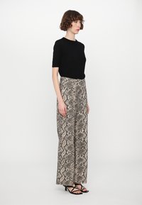 Top nero a maniche corte abbinato a pantaloni beige a gamba larga con motivo a stampa serpente. Sandali neri con tacco completano l'outfit.