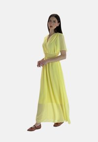 Robe maxi de couleur jaune vif, en tissu léger avec un décolleté en V et de courtes manches volantées. Présente une taille smockée et une jupe fluide.