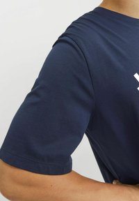 Donkerblauwe T-shirt met korte mouwen en een ronde halslijn van gladde katoenen stof. Heeft een wit grafisch ontwerp over de borst.