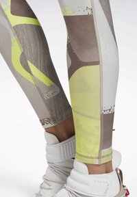 Ben med mönstrade leggings i gult, brunt och vitt samt vita Reebok högstövelskor.