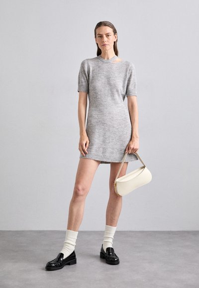 Robe tricotée grise à manches courtes et décolleté. Associée à des mocassins noirs, des chaussettes blanches et un sac à main blanc. Texture lisse.