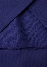 Námořnická modrá látka s texturovaným pleteným vzorem, s hladkými žebrovanými akcenty na okrajích a švech. Materiály vypadají měkké a elastické.