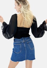 Top nero smockato con maniche a sbuffo trasparenti, abbinato a una minigonna in denim blu con orlo sfrangiato e tasche posteriori tradizionali.
