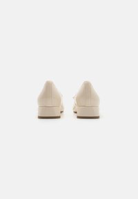 Chaussures en faux cuir beige avec un petit talon carré, texture lisse, design minimaliste et bout légèrement pointu. Vue de dos.