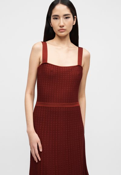 Πλεκτό φόρεμα χρώματος τούβλο με τετράγωνο ντεκολτέ, φαρδιές τιράντες και εφαρμοστό μπούστο. Η υφή έχει ένα διακριτικό ραβδωτό μοτίβο.