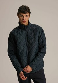 Pikowana ciemnoniebieska kurtka z wysokim kołnierzem, przednim zamkiem błyskawicznym i długimi rękawami. Posiada wzór w diamenty i luźny krój.