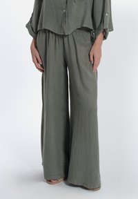 Outfit leggero in lino di colore verde oliva, composto da una blusa morbida con bottoni e pantaloni a gamba larga con cintura elastica e tessuto lavorato.