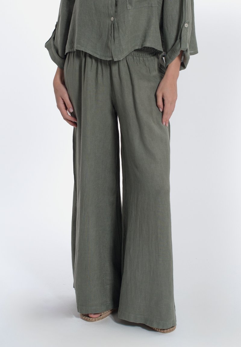 Outfit leggero in lino di colore verde oliva, composto da una blusa morbida con bottoni e pantaloni a gamba larga con cintura elastica e tessuto lavorato.