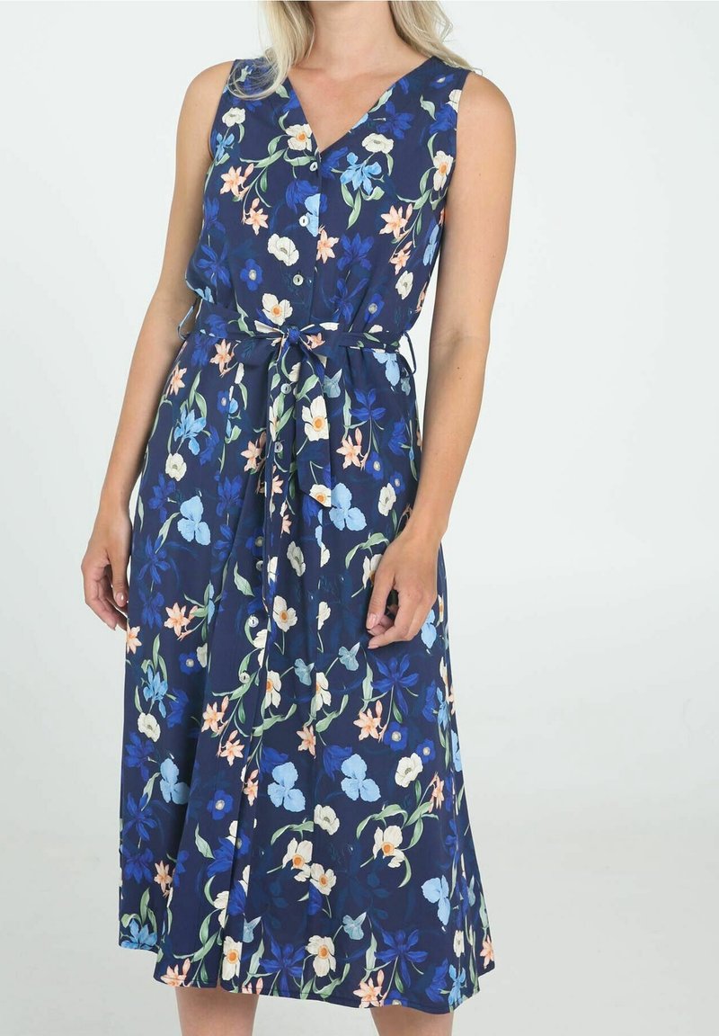 Robe bleu marine sans manches avec motif floral multicolore, boutonnée à l'avant, ceinturée à la taille, portée par une femme debout.