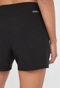 Sorte svømmeshorts med en glat tekstur, med baklomme og logo detalj nær midjebåndet. Enkelt design, lengde til midten av låret.