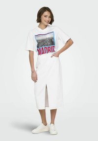Witte katoenen t-shirt met een grafische print van "Madrid" in rood en blauw, gecombineerd met een witte, knie-lange rok en witte sneakers.