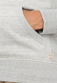 Gray hoodie with textured fabric, featuring a front pocket and ribbed cuffs. Small tag with "BLEND 1993" visible on the lower seam.