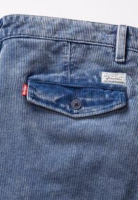 Poche arrière d'un pantalon en velours côtelé bleu avec rabat à bouton, onglet rouge Levi's et étiquette de marque blanche sur la ceinture.