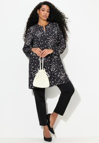 Czarna tunika z białym nakrapianym wzorem, z przodu na guzik, z długimi rękawami. Połączona z czarnymi spodniami i białą torbą na sznurku.