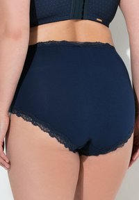 Mutandine alte navy in vita con rifiniture in pizzo lungo le aperture delle gambe, realizzate in un tessuto morbido e liscio. Caratterizzate da una vestibilità aderente e da una copertura minima.