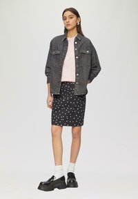 Een donkergrijze spijkerjack, gecombineerd met een lichtroze T-shirt en een zwarte rok met witte stippen. Zwarte chunky schoenen en witte sokken.