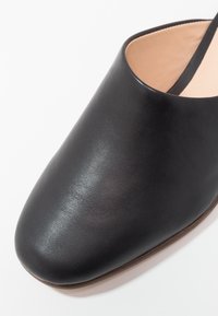 Chaussure en cuir noir à enfiler, à texture lisse et bout arrondi. L'intérieur est doublé d'un beige clair et la semelle est plate.