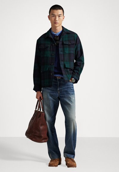 Zöld és sötétkék kockás dzseki, sötét pulóver, kopott kék farmernadrág, barna bőrtáska és bézs lábbeli. Kényelmes stílus, több zsebbel.