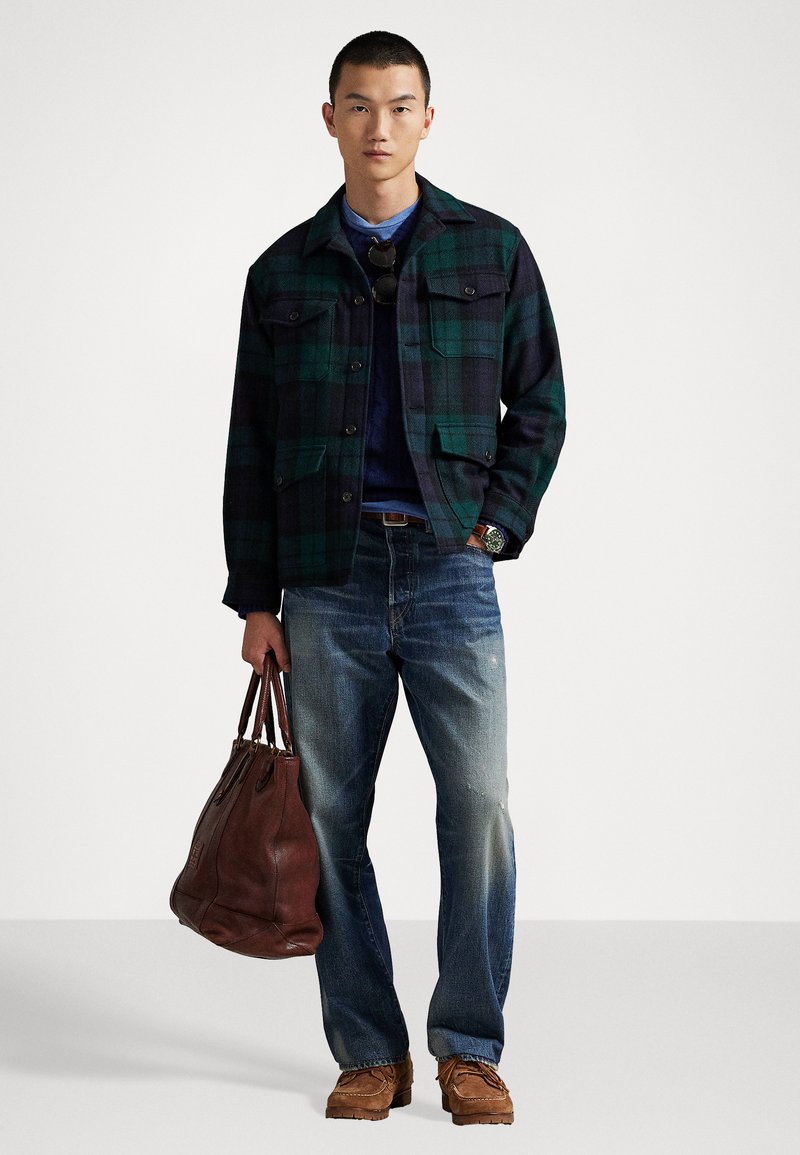 Grøn og navy plaid jakke, mørk sweater, slidte blå jeans, brun lædertaske og tan-farvet fodtøj. Afslappet stil med flere lommer.