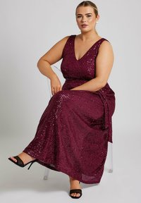 Vestido de lentejuelas burdeos con escote en V profundo, tejido texturizado, cintura ajustada y falda fluida. Llevado con tacones abiertos negros.