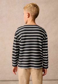 Fekete-fehér csíkos, hosszú ujjú ing, puha anyagból, kerek nyakkivágással, laza szabással, világos színű nadrággal párosítva.