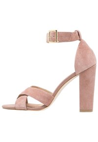 Rosa mocka högklackad sandal med korsade tåremmar, vristrem och guldspänne, med en blockklack.