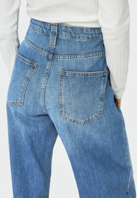 Traperice s visokim strukom u plavoj boji, meke teksture, s dva stražnja džepa i kontrastnim detaljima šivanja.