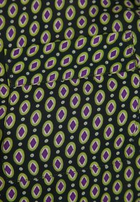 Primo piano di un tessuto nero con un motivo ovale verde e un diamante viola, dotato di una tasca rettangolare cucita.