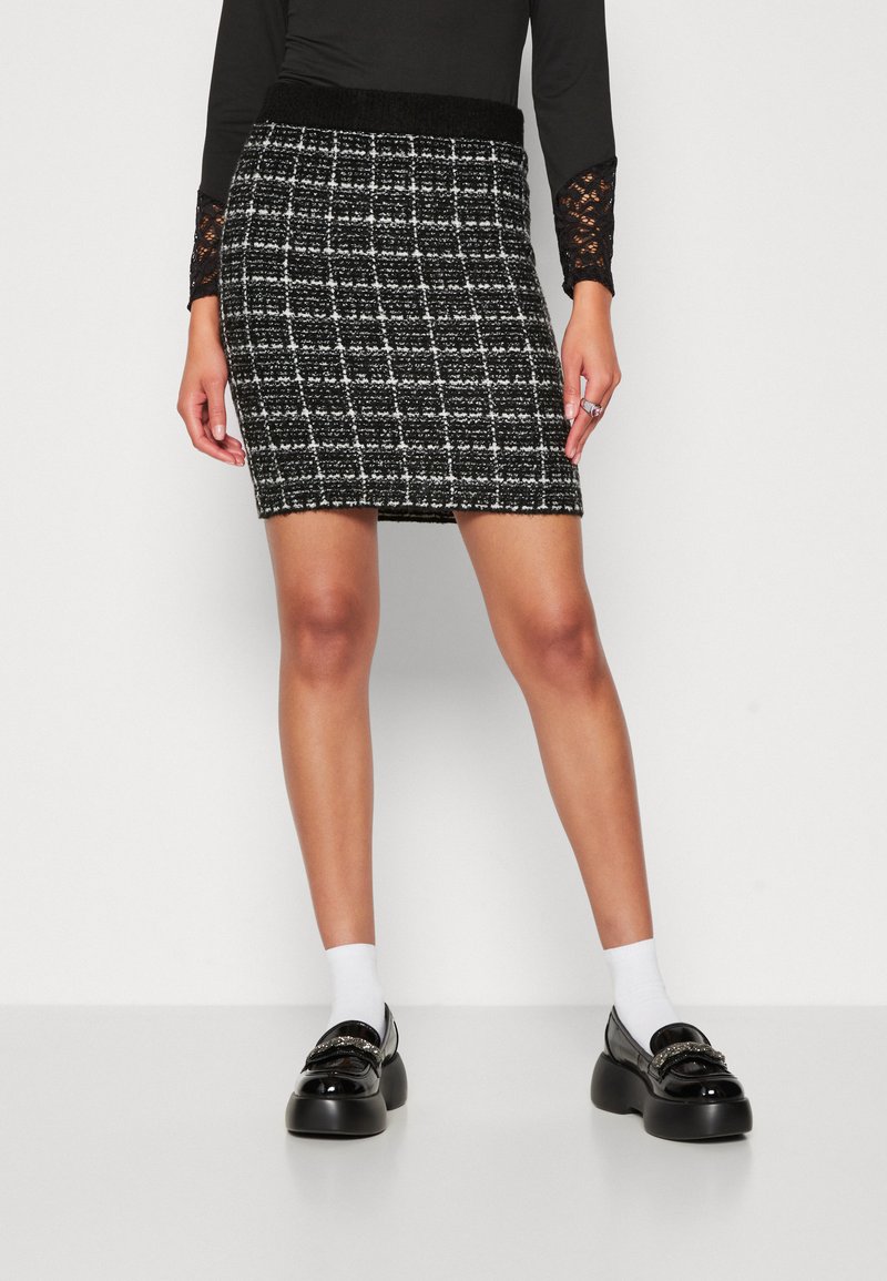 Černobílá tweedová miniskirt s texturovaným povrchem a elastickým pasem. Stylizováno s černými botami a bílými ponožkami.
