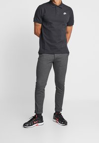 Svart Nike pikétröja, grårandiga byxor och svarta sportskor med röda accenter. Enkel, figursydd design med klassisk krage.