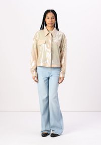 Sequined cropped jacket in light beige, with a collared neckline and two front pockets; paired with light blue flared jeans and black flats.