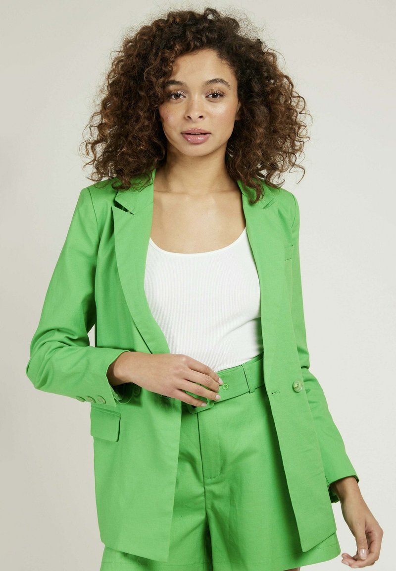 Ensemble de blazer et de short vert en tissu léger. Le blazer présente des revers et des fermetures à boutons ; le short a une ceinture assortie et des poches.