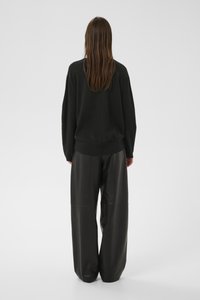 Must oversized kampsun tekstureeritud kudumiga, kombineeritud kõrge vöökohaga mustade nahast pükstega, millel on laiad sääred ja sile viimistlus.