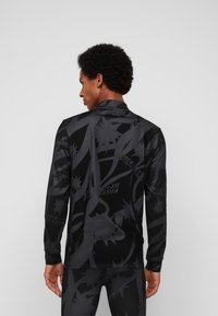 Langärmliges Sportshirt in Schwarz mit abstrakten Mustern und schmaler Passform. Hergestellt aus einem glatten, elastischen Stoff mit Stehkragen.