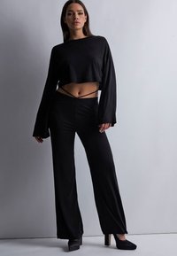 Haut noir à manches longues cropped avec une coupe décontractée, assorti à un pantalon noir taille haute à jambes larges. Tissu texturé avec des coutures minimales.