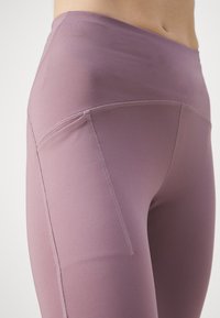Leggings deportivos de cintura alta en un color lavanda suave, fabricados con un tejido elástico, que cuentan con un bolsillo lateral y costuras planas.