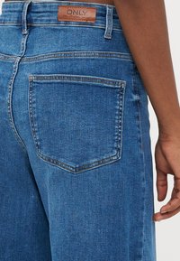 Modri jeans iz denima z ohlapnim krojem, ki se ponašajo z usnjeno etiketo na pasu in zanjim žepom.