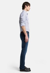 Camicia a righe azzurro chiaro con bottoni, jeans blu scuro, scarpe nere. Taglio slim, maniche lunghe arrotolate, tessuto denim, senza motivi visibili.