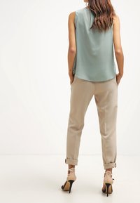 Top senza maniche di un verde chiaro elegante abbinato a pantaloni beige a sigaretta, presentato con sandali con tacco aperto sul retro.