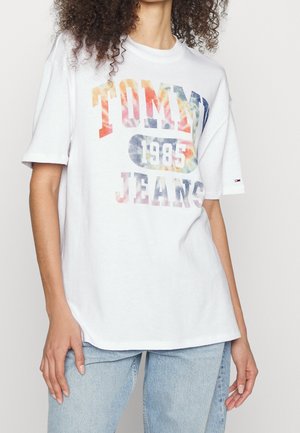 Biała bawełniana koszulka z kolorowym nadrukiem "TOMMY JEANS 1985", krótkie rękawy, luźny krój i proste wykończenie u dołu.