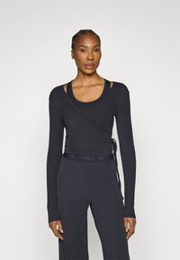 Fekete, hosszú ujjú átlapolt felső testhez simuló szabással, puha tapintású anyagból, derékrésznél megkötővel, fekete trikó fölé viselve.