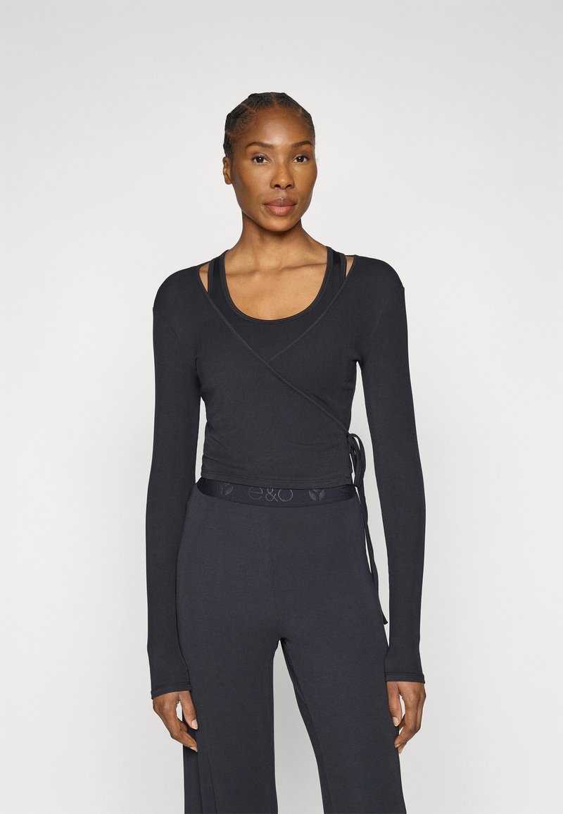 Fekete, hosszú ujjú átlapolt felső testhez simuló szabással, puha tapintású anyagból, derékrésznél megkötővel, fekete trikó fölé viselve.