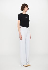 Black fitted t-shirt with "MAX&Co" logo, paired with high-waisted, wide-leg white trousers. Simple design with pockets and a button.