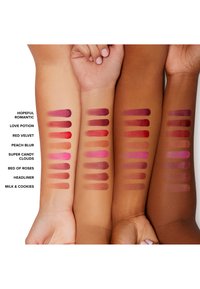 Swatches of lip colors on diverse skin tones. Colors include pink, red, and mauve shades in varying finishes, labeled with product names.