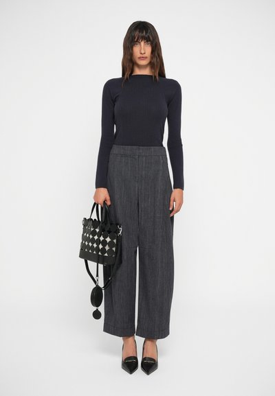 Haut long à rayures navy, pantalon large gris à rayures, sac à main noir à motifs géométriques et escarpins noirs pointus.